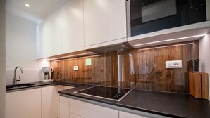 A modern kitchen with white cabinetry, a black countertop, and a wood panel backsplash. - 179A Apartments Seida (Selva di Val Gardena)