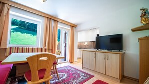 A modern kitchen with a flat-screen TV, wooden cabinets, and a dining area with a table and chairs. - 179A Apartments Seida (Selva di Val Gardena)