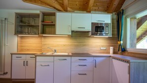 Una cocina moderna con armarios blancos, un microondas de acero inoxidable y techo de madera.