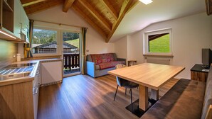 Una cocina moderna con vigas de madera, un comedor con mesa y banco, y un sofá con vista al exterior.