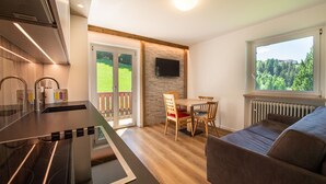 Een moderne keuken met een inbouwfornuis, een eethoek met een tafel en stoelen, en een groot raam met uitzicht op groen.