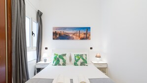 A hotel room with a bed, two nightstands, a painting of a beach scene, and a window with curtains.