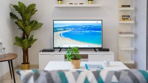 A modern living room with a flat-screen TV displaying a beach scene, a potted plant, a coffee cup, and a bookshelf.