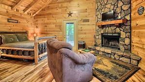 A cozy log cabin interior with a stone fireplace, a television mounted above it, and a comfortable seating area with a sofa and a chair. - Destiny's Daydream - Couple's Cabin- Hocking Hills (Logan)