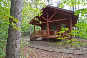 Une cabane en bois avec un porche, entourée d’arbres.