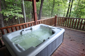 A hot tub on a wooden deck surrounded by a forest.