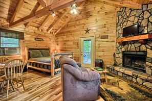 L’intérieur d’un chalet confortable, avec des murs en rondins de bois, une cheminée en pierre, des meubles en bois et une grande fenêtre.