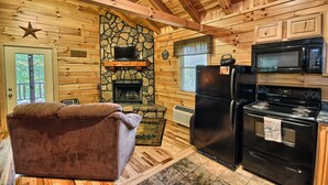 A cozy cabin interior with a stone fireplace, a television, a refrigerator, and a kitchen area. - Destiny's Daydream - Couple's Cabin- Hocking Hills (Logan)