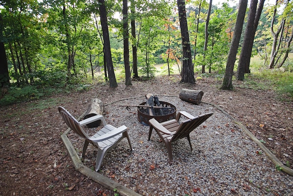 A forested area with a fire pit and two chairs.