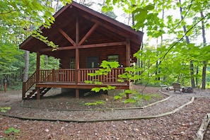 A wooden cabin with a porch, surrounded by trees.
