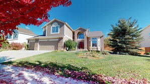 A two-story house with a garage, a front yard with a lawn, and a large evergreen tree.