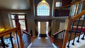 A grand staircase with a view of the upper floor, a large arched window, and a wooden railing.