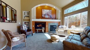 A spacious living room with a fireplace, comfortable seating, and a large window offering a view of the outdoors.