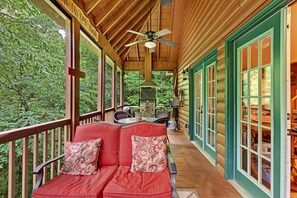 A covered porch with a red sofa, a ceiling fan, and a grill. - Cabin Helen's Hideaway (Helen)