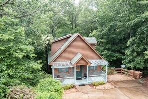 A cabin with a porch, surrounded by dense forest. - Cabin Helen's Hideaway (Helen)