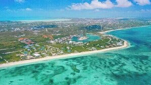 Vista aérea de una zona costera con playa, aguas cristalinas y una combinación de edificios residenciales y comerciales.