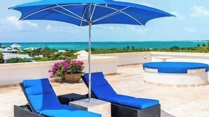 Terraza en la azotea con dos sillones azules y una gran sombrilla azul.