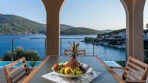 Une table avec un panier de fruits, deux chaises en bois et une vue sur un lac et des collines.