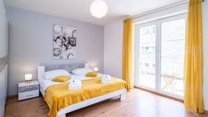 A modern bedroom with a bed, bedside tables, a wall art piece, and a large window with yellow curtains.