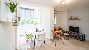 A modern living space with a dining area, a sofa, a TV, and a plant.