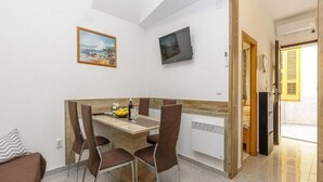 A dining area with a wooden table, four chairs, a painting, and a TV on the wall. - Apartment Senj - Two Bedroom Apartment (Senj)
