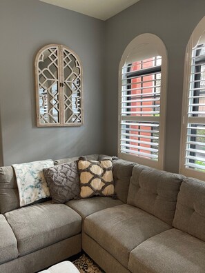 Relax on a beige sectional sofa in a cozy room with a gray wall and a window offering a view of the city.