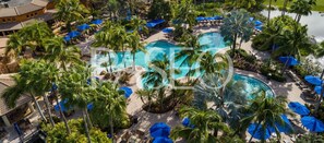 An aerial view of a resort with multiple swimming pools, palm trees, and lounge areas.