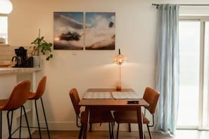 Un comedor con una mesa de madera, cuatro sillas, una lámpara y dos cuadros colgados en la pared.