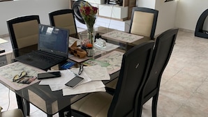 Un coin repas avec une table en verre, des chaises noires, un ordinateur portable et un vase rempli de fleurs.