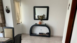 Un coin repas avec une table et des chaises, une console sur laquelle sont posées des chaussures, une plante en pot et un miroir au mur.