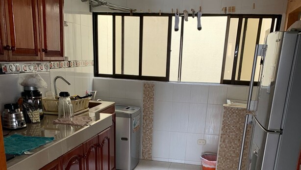 Une cuisine avec des meubles de rangement en bois, un évier, un lave-linge et un réfrigérateur.