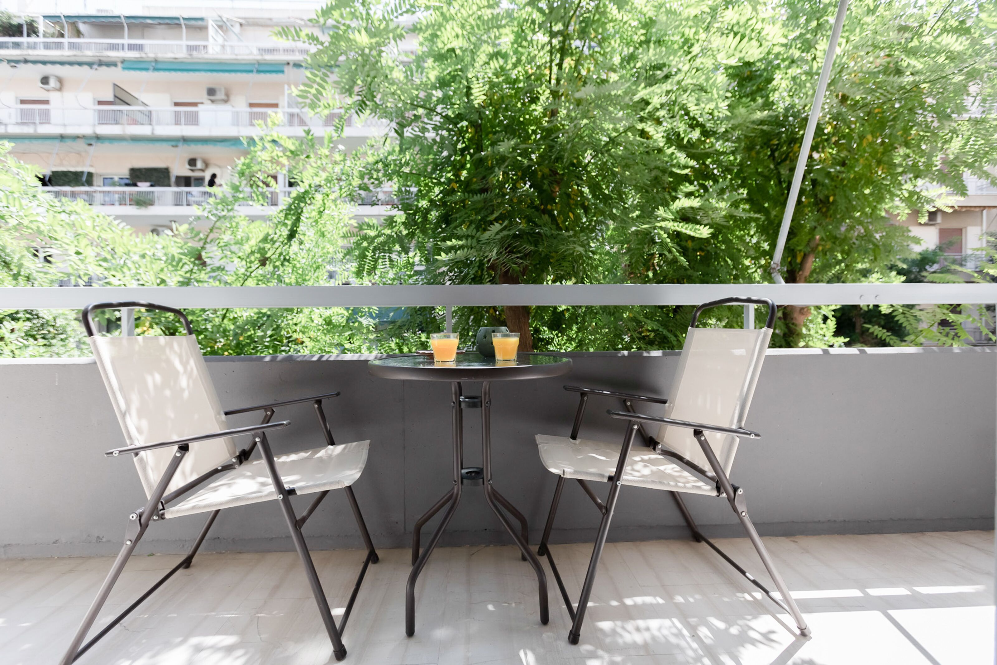 A balcony with two foldable chairs and a small table, a glass of orange juice, and a glass of water.