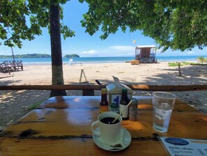 Une table installée sur la plage, avec un menu, des condiments et une boisson.