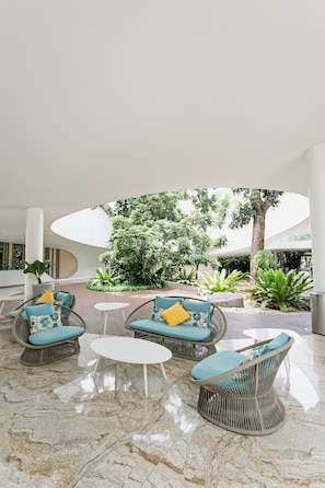 Relax in a serene indoor lounge with wicker chairs, a round table, and lush green views.