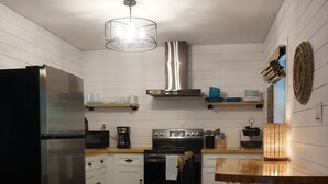 Une cuisine moderne avec des meubles blancs, un réfrigérateur en acier inoxydable, une cuisinière noire et un îlot central en bois doté d’un tabouret de bar.