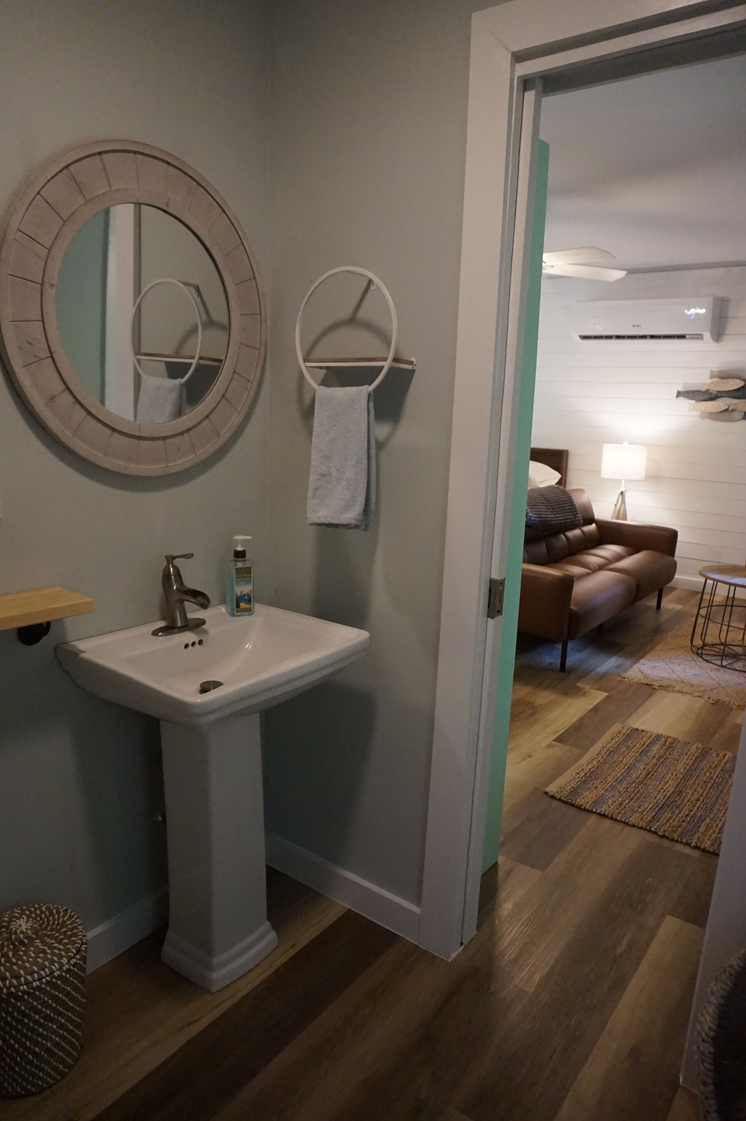 Une salle de bain avec un lavabo sur colonne, un miroir rond et une serviette accrochée au mur.