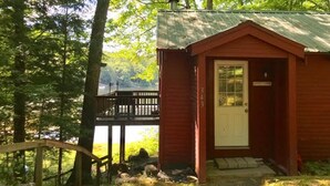 A small, single-story cabin with a red exterior, a white door, and a small porch area. - Cozy Cabin on Loon Lake (Plymouth)
