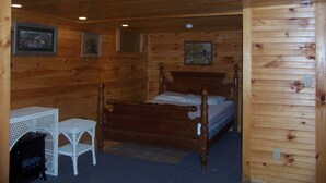 A wooden cabin bedroom with a four-poster bed, a small table, and a fireplace. - Cozy Cabin on Loon Lake (Plymouth)