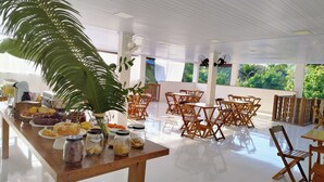 A spacious room with a long wooden table set with breakfast items, surrounded by wooden chairs. - Pousada Cantinho do Sossego em Paraty (Paraty)