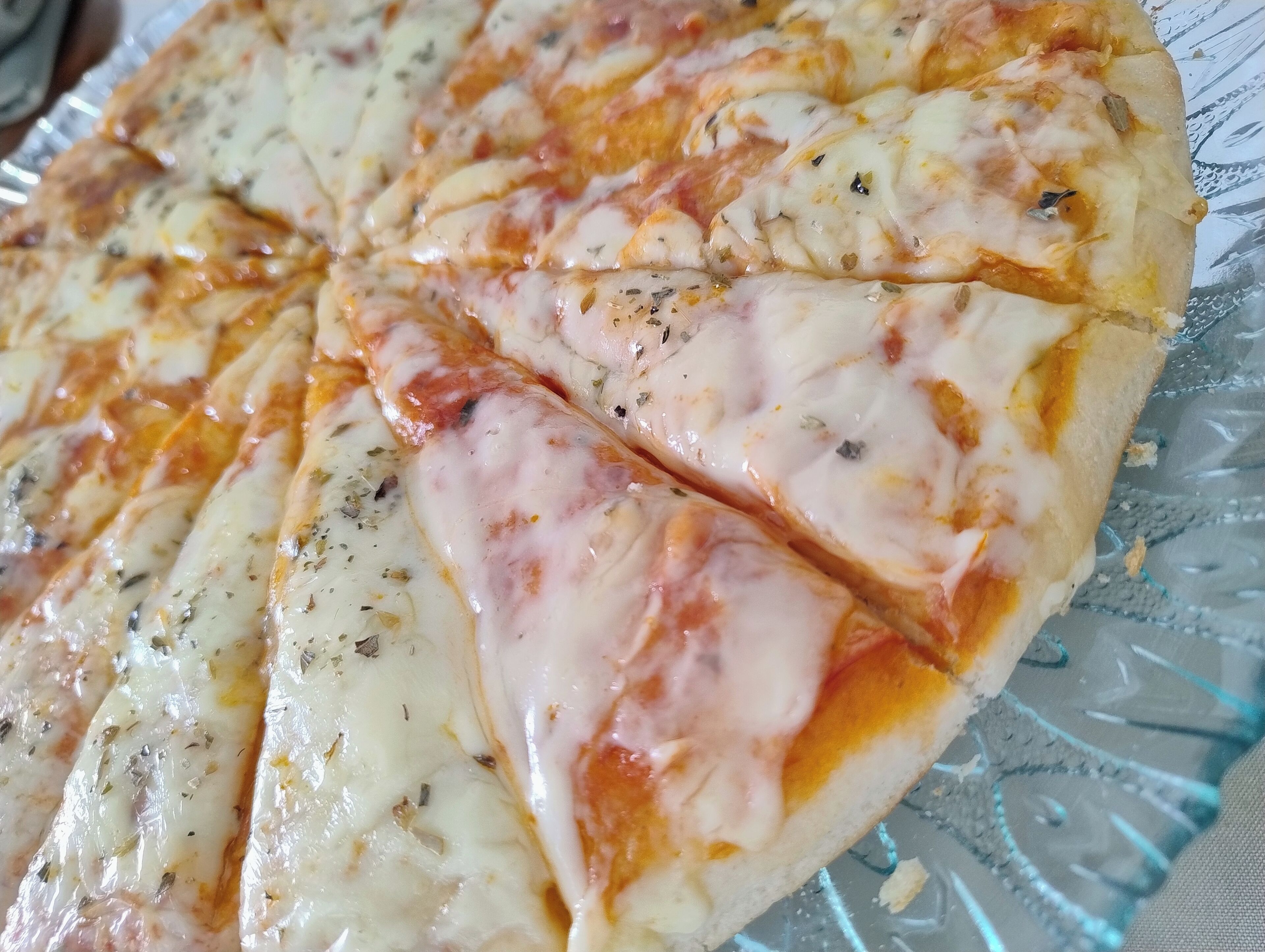 A pizza with visible herbs and cheese on a glass plate.