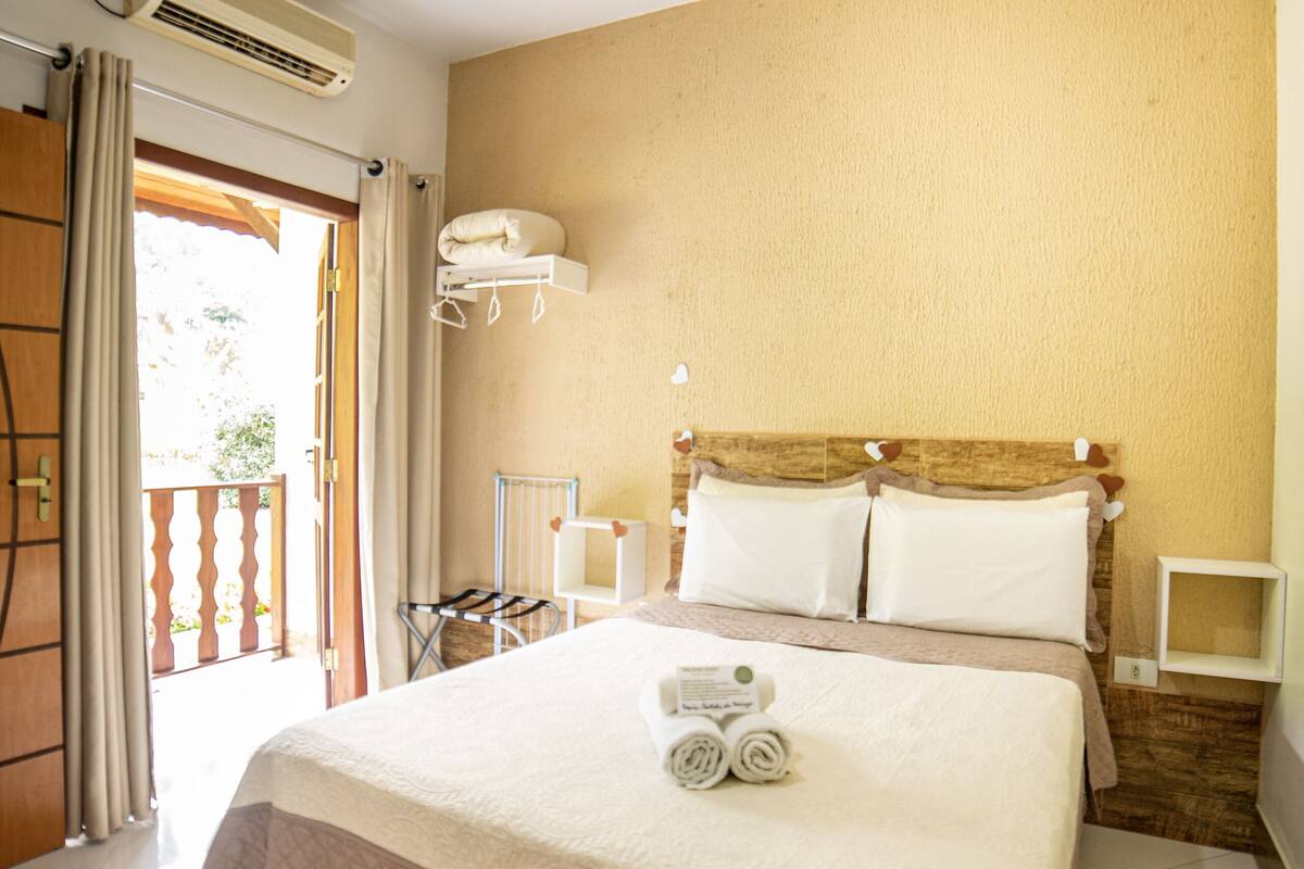 Ein Hotelzimmer mit Bett, Deckenventilator, Klimaanlage, kleinem Tisch und einem Fenster mit Vorhängen.