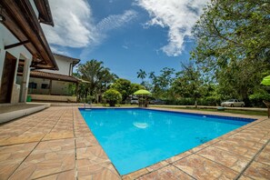 Une piscine dotée d’une terrasse carrelée, entourée de verdure et bordée d’un bâtiment dont le toit est également recouvert de tuiles.