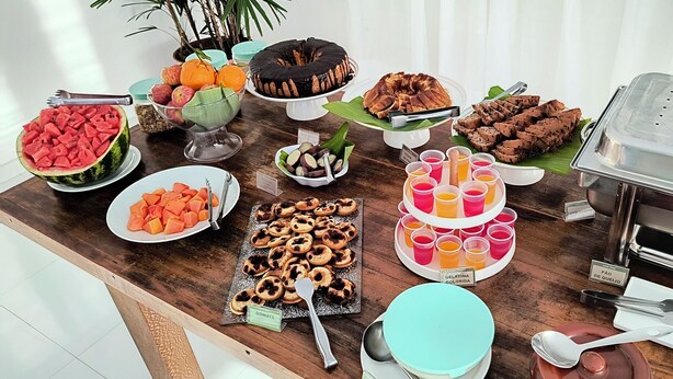 A buffet table with various food items including watermelon, apples, oranges, a chocolate cake, and several trays of desserts. - Pousada Cantinho do Sossego em Paraty (Paraty)