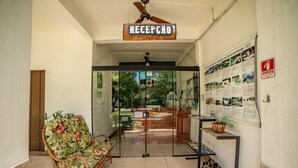 A reception area with a sign reading "RECEPCAO," a wicker chair, a small table with a plant, and a bulletin board with various notices. - Pousada Cantinho do Sossego em Paraty (Paraty)