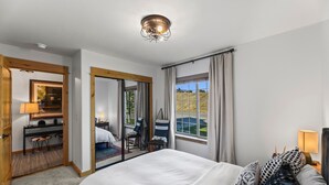 A hotel room with a large bed, a desk with a lamp, a chair, and a view of a grassy area through the window. - Montana Adventure Living - Close to Yellowstone & Downtown Livingston (Livingston)
