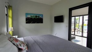 A bedroom with a bed, a painting, a television, and a sliding door to a balcony. - Coconut Life Cabinas "Rockford" -  One Bedroom, Close to Store, Town and Beach (Sámara)