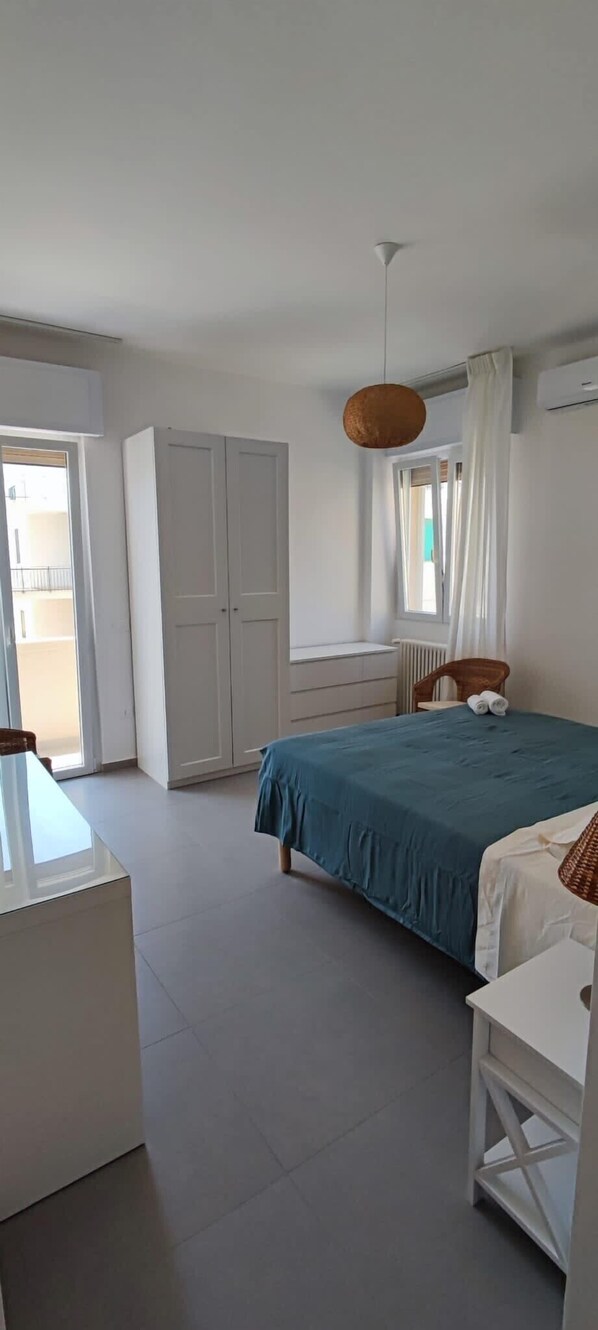 A bedroom with a bed, a desk, a wardrobe, and a window with curtains.