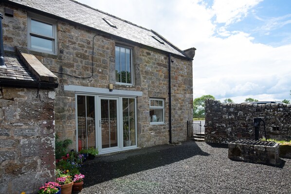 A stone building with a gravel driveway, a large glass door, and potted plants.
