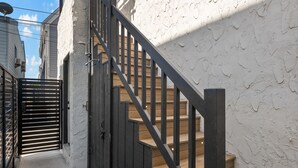 A narrow outdoor staircase with wooden steps and black metal railings leading to a gated entrance. - Modern Retreat Steps to the Beach! (San Diego)