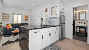 A modern kitchen with white cabinets, a black marble island, and a stainless steel refrigerator. - Modern Retreat Steps to the Beach! (San Diego)